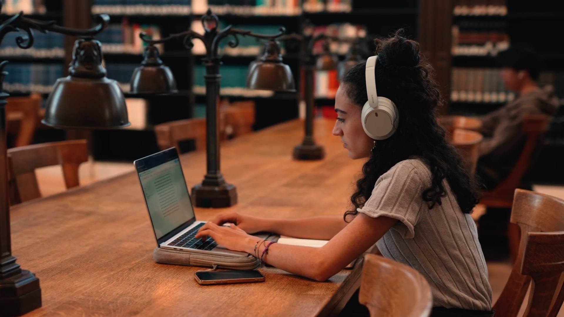 Student wearing headphones and using a laptop at a library table
