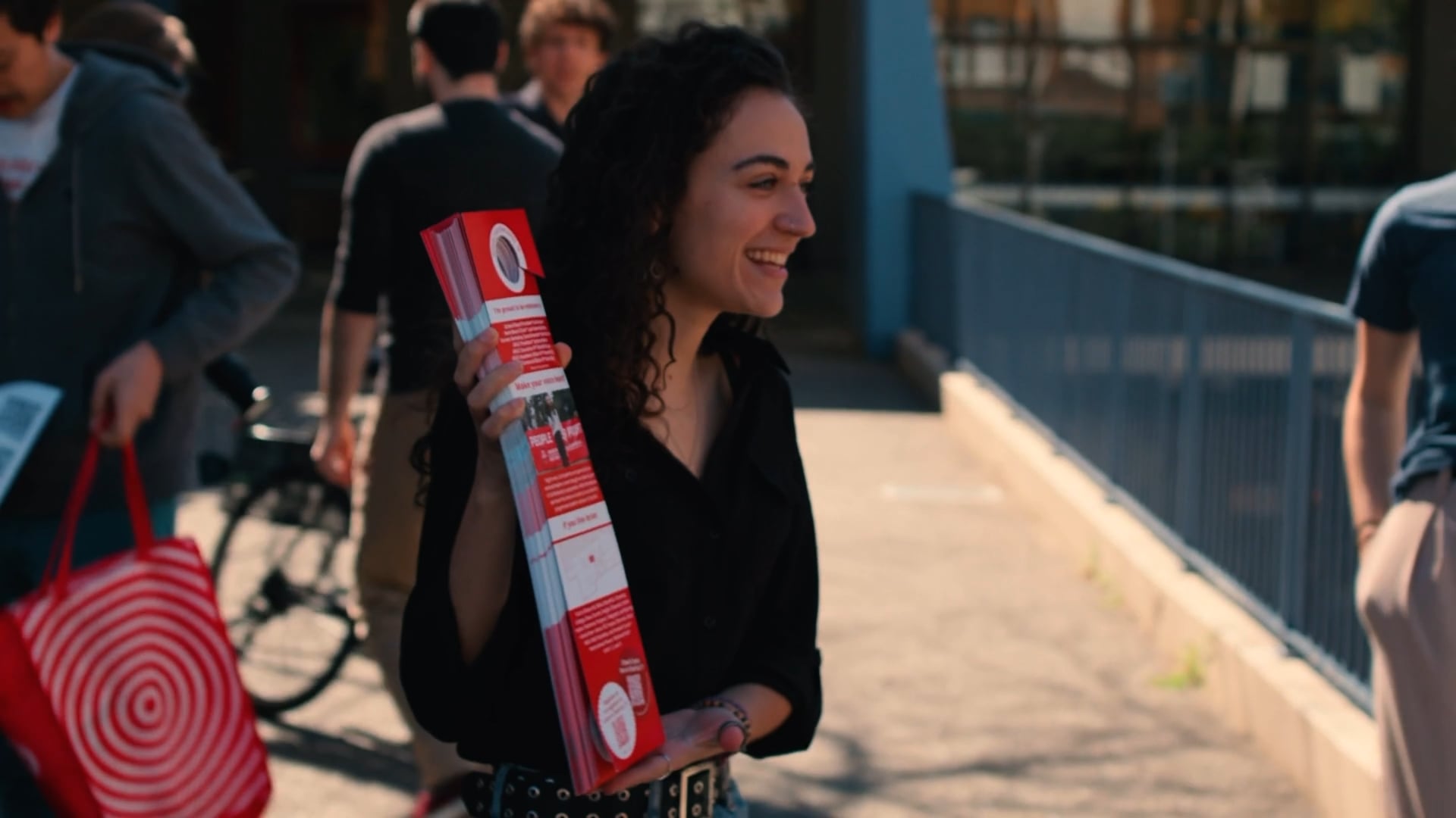 Smiling supporter holding a rolled campaign sign on a pedestrian bridge