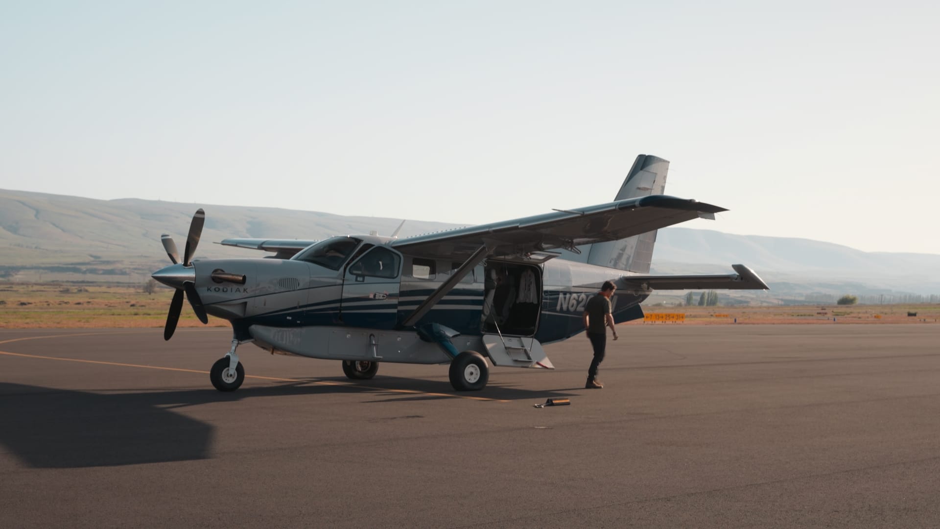 Small Kodiak turboprop plane parked on a runway with hills in the background
