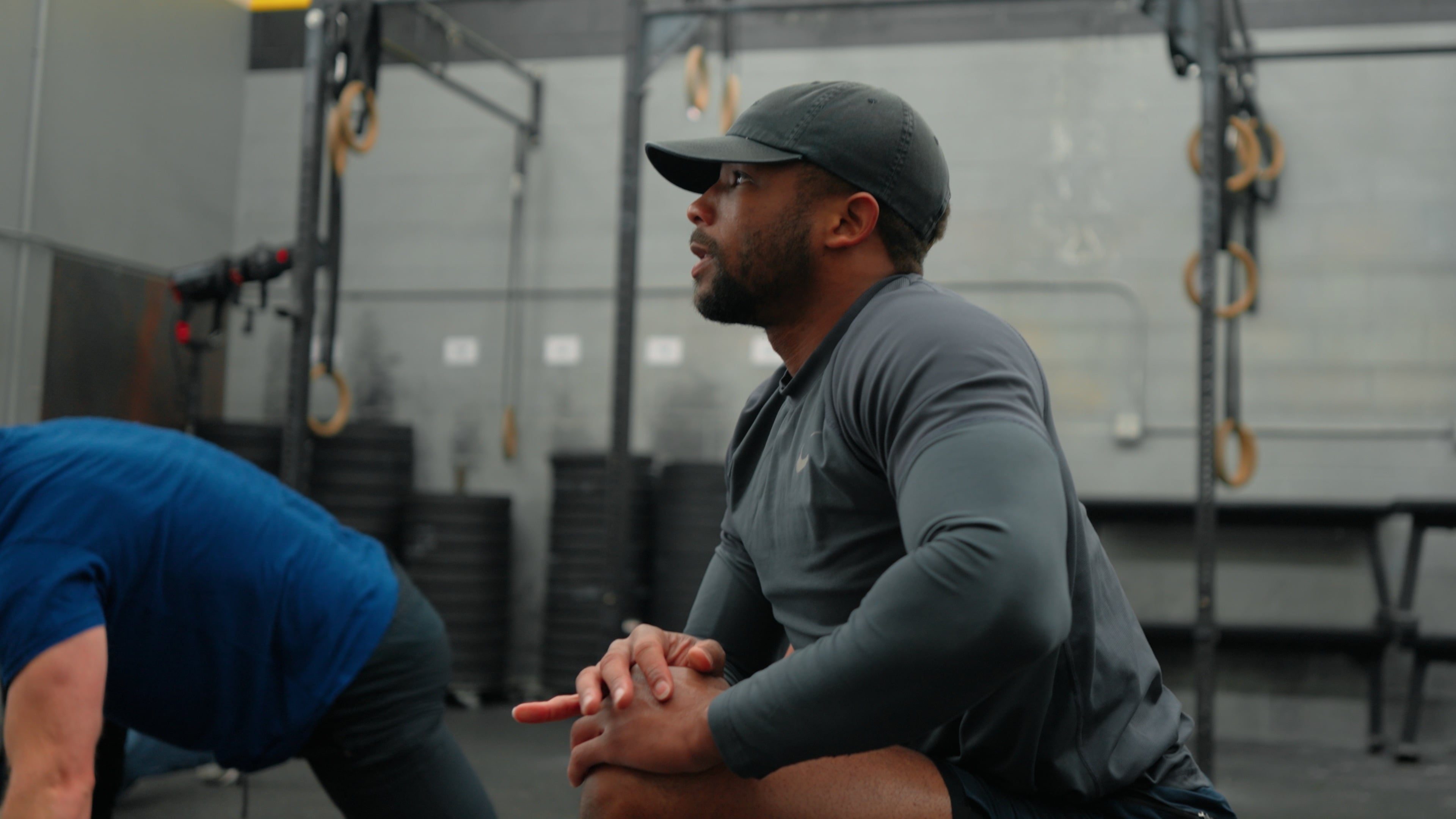 Member with hands clasped resting between sets, gym rings visible behind him