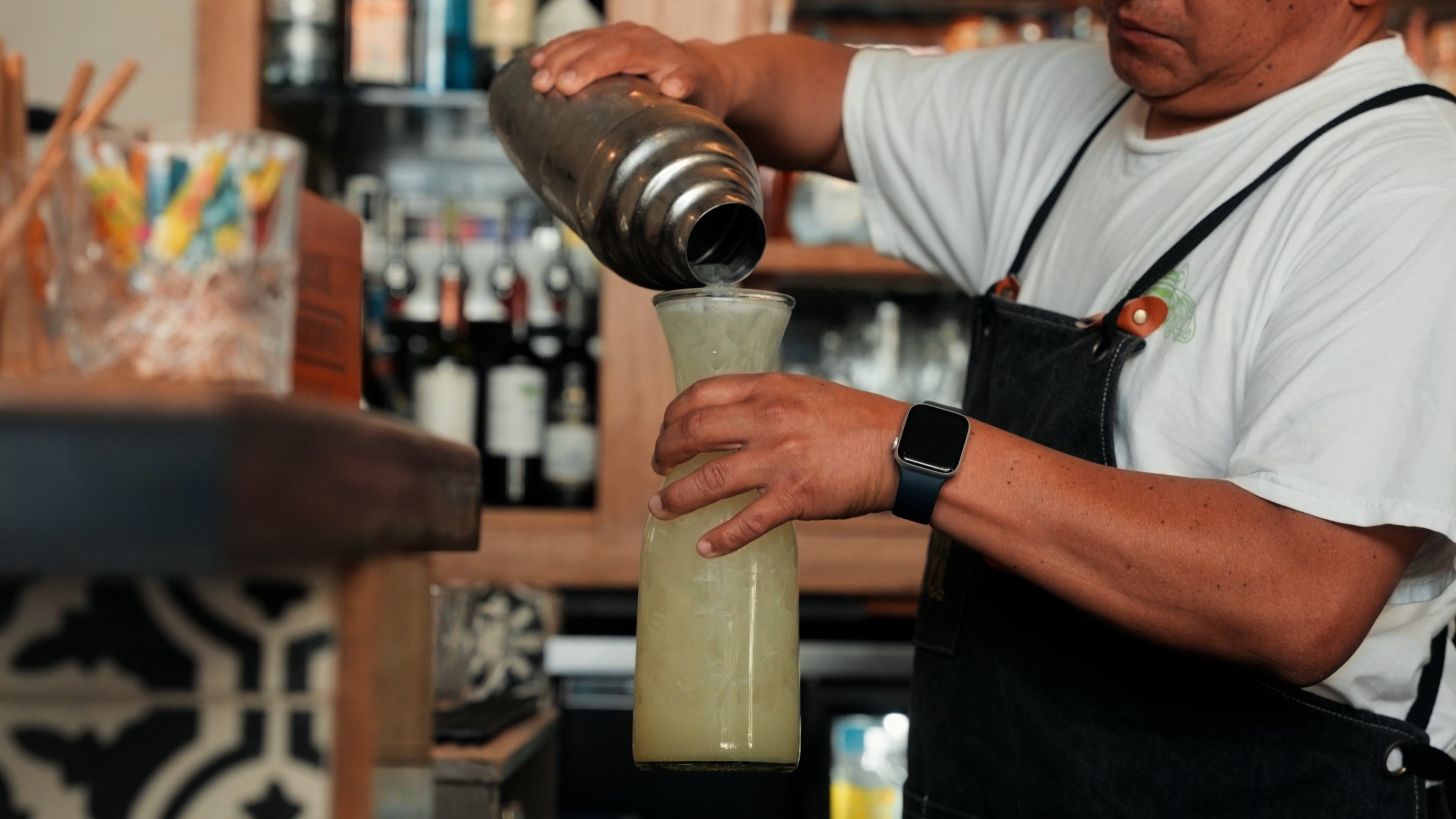 Bartender pouring a cocktail into a glass carafe over ice