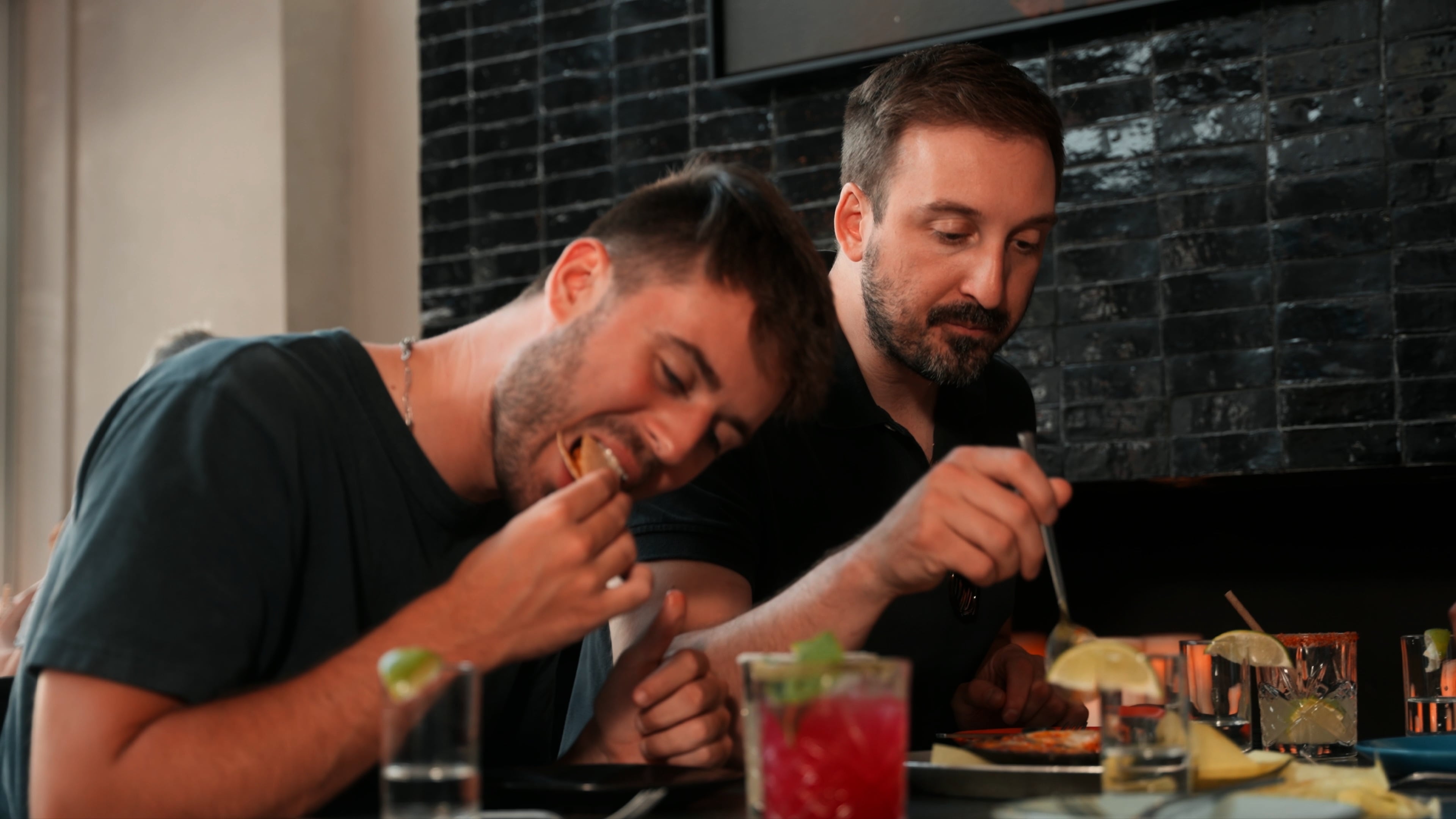 Two diners eating tacos and drinks at the bar