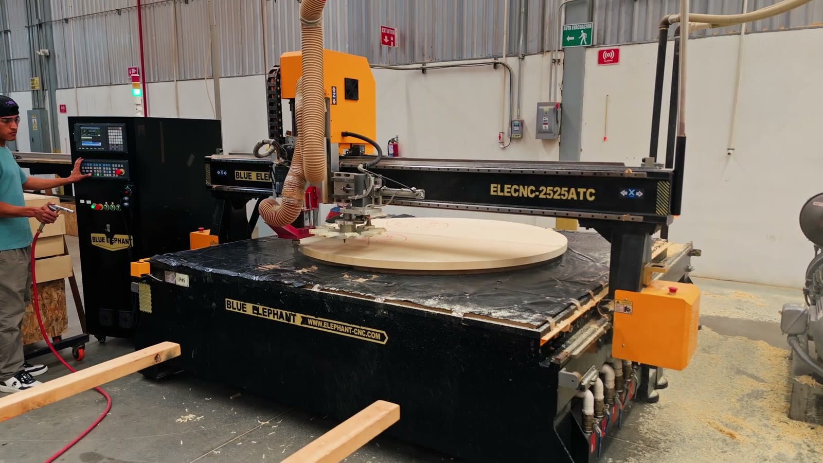 A worker beside a CNC router cutting a large round panel of wood