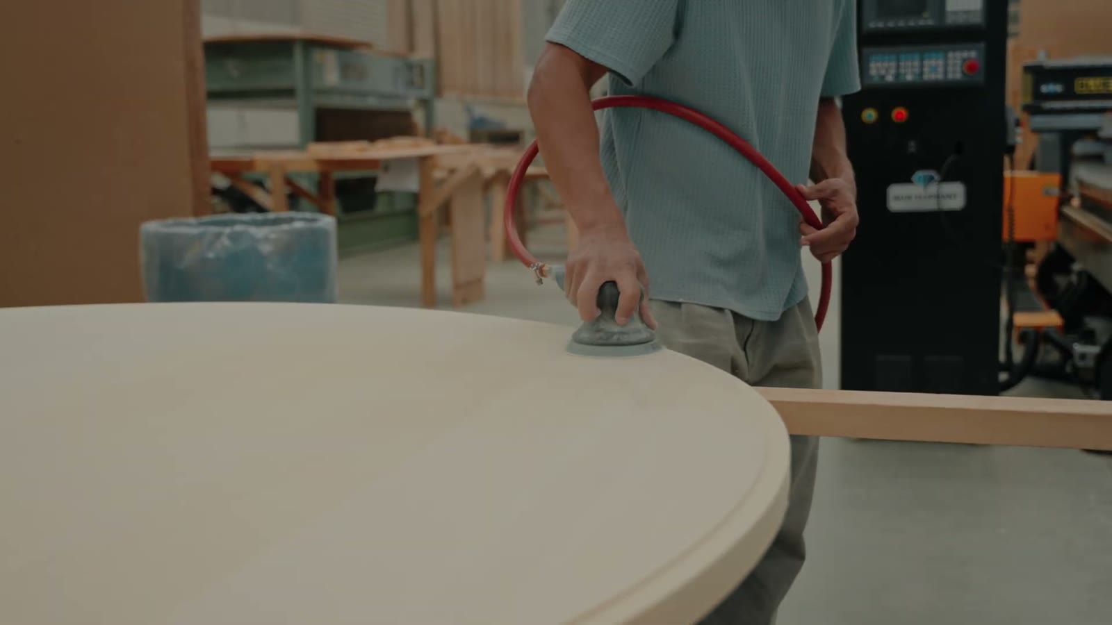 A worker sanding the edge of a large round wooden tub base